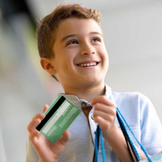 A young boy smiling as he holds up a plain green card in one hand and shopping bag straps in the other.